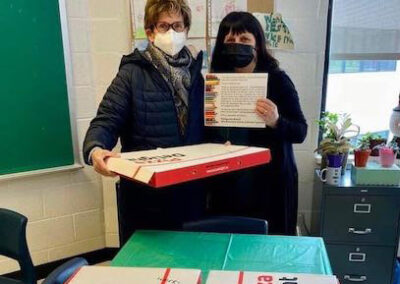Two women standing in front of a table holding a pizza box